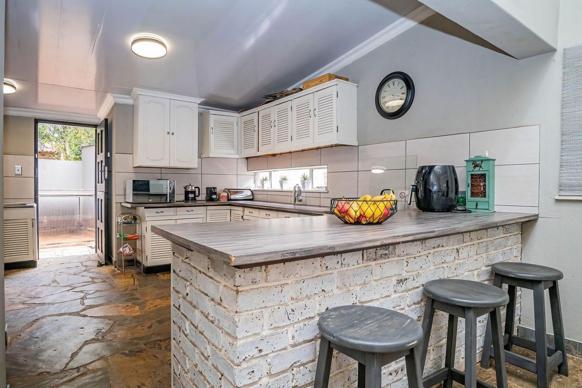 A functional kitchen featuring white cabinetry, a rustic brick breakfast bar, stone flooring, and a tiled backsplash with direct access to an outdoor area.