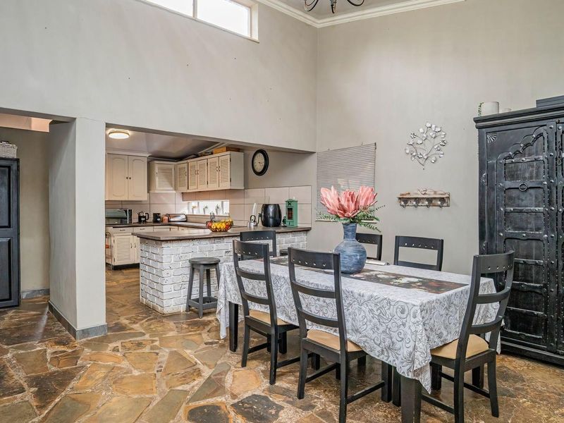 Open plan dining area featuring rustic stone flooring and high vaulted ceilings, seamlessly connected to a functional kitchen with a brick breakfast bar.