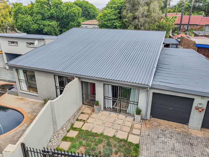 Aerial view of a modern home featuring a corrugated metal roof, a swimming pool, paved patio area, and a double garage with paved driveway.