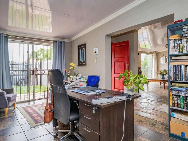 A functional home office space featuring tiled flooring, a sliding glass door with security gate, and direct access to an adjacent living area.