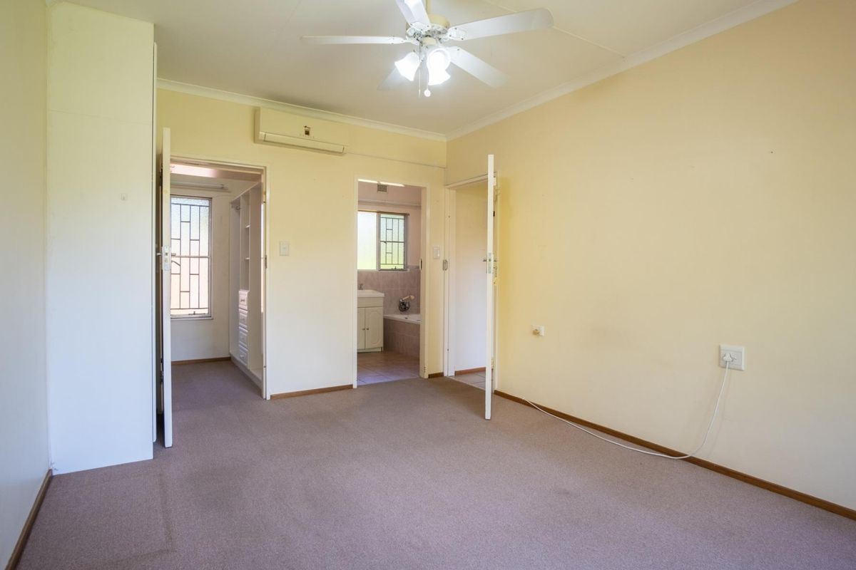 Spacious bedroom featuring neutral walls, carpet flooring, a ceiling fan, and an integrated air conditioning unit, with direct access to an en-suite bathroom.