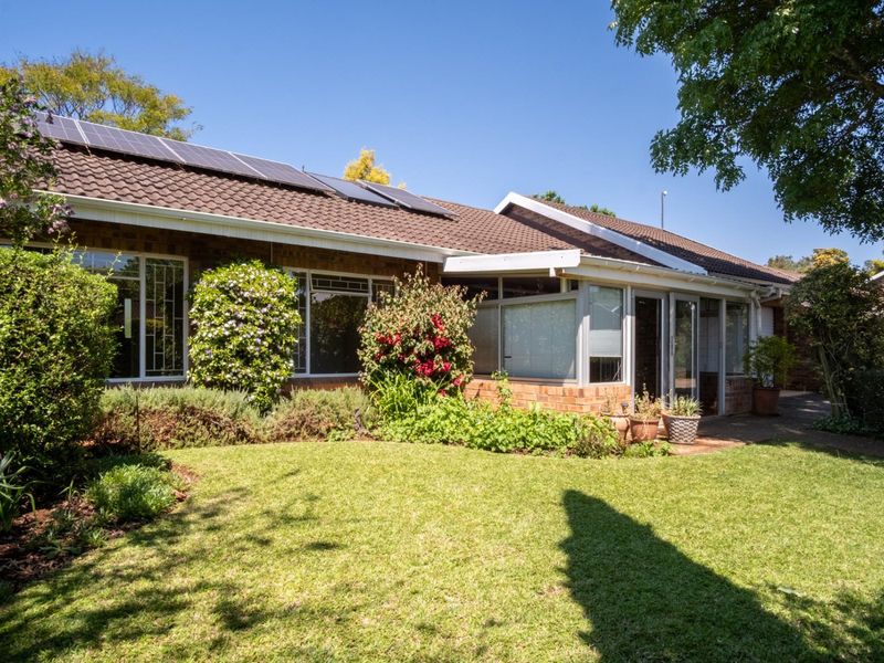Rear view of the townhouse featuring a well-maintained garden, brick exterior, tiled roof with solar panels, and an enclosed patio area.