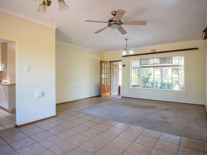 Spacious open-plan living area featuring a combination of tiled and carpeted flooring, ceiling fan, and direct access to a functional kitchen.