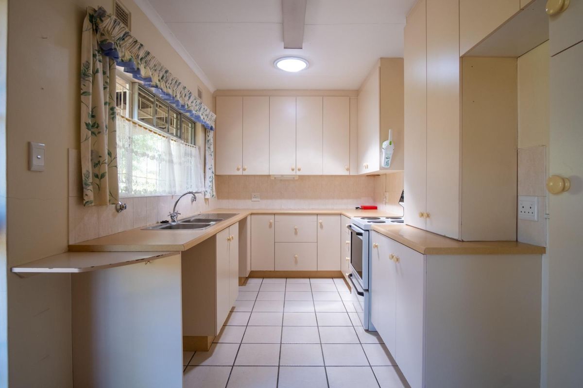 A functional kitchen featuring laminate countertops, double bowl sink, and ample built-in cabinetry, offering a clean layout ready for modern updates.