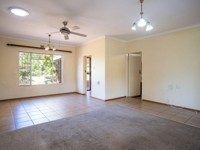 Spacious living area featuring a combination of tiled and carpeted flooring, ceiling fan, and large windows with security bars.