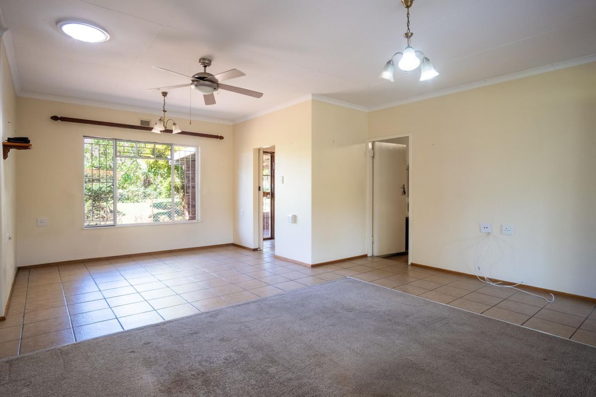 Spacious living area featuring a combination of tiled and carpeted flooring, ceiling fan, and large windows with security bars.