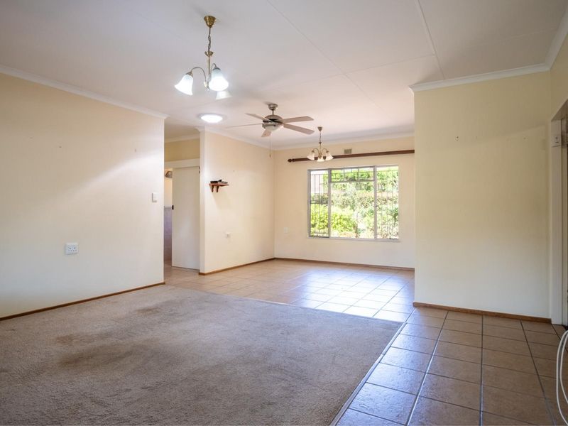 Spacious open-plan living area featuring a combination of carpeted and tiled flooring, ceiling fan, and large windows with security bars.