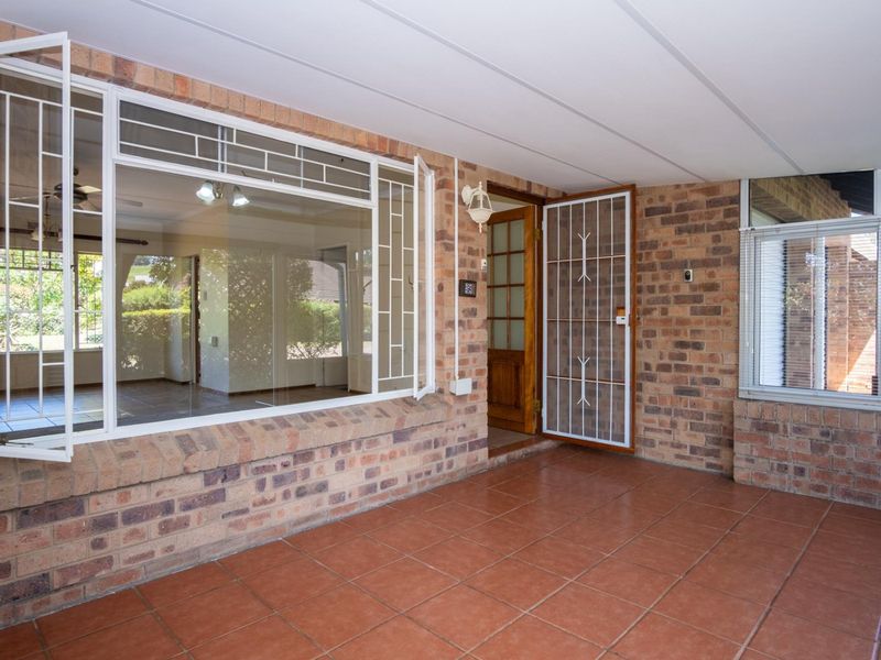 A covered patio area featuring exposed brick walls, tiled flooring, and a secure entrance door, providing a functional outdoor transition space.