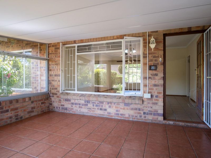 A spacious, enclosed patio area featuring exposed brick walls, tiled flooring, and large windows, providing a bright and versatile transition space.