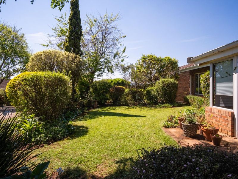 A well-maintained private garden featuring a lush lawn, mature shrubbery, and a paved patio area adjacent to the townhouse brick facade.