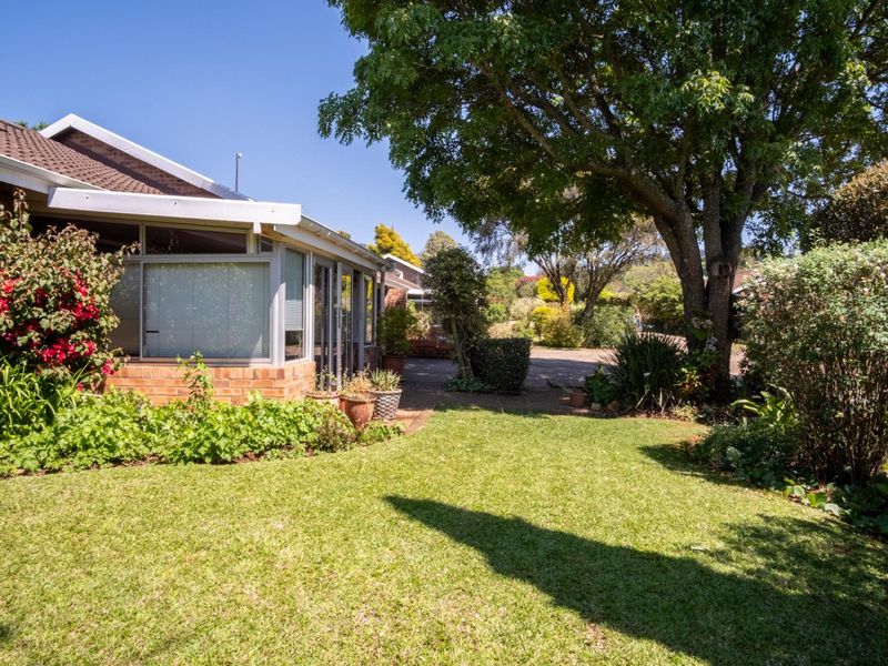 A well-maintained rear garden featuring a paved patio area, established trees, and a brick townhouse facade with aluminium window frames.