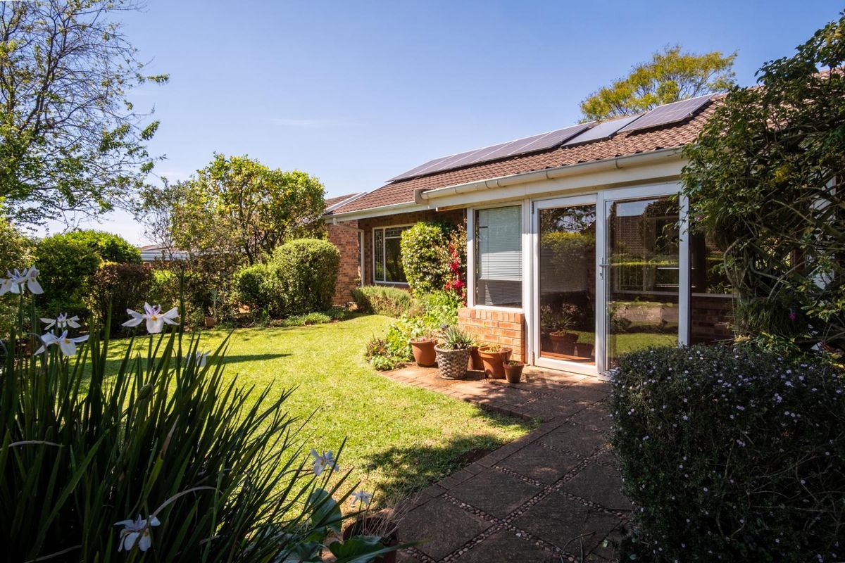 Rear view of the townhouse featuring a well-maintained garden, paved walkway, sliding glass doors, and roof-mounted solar panels.