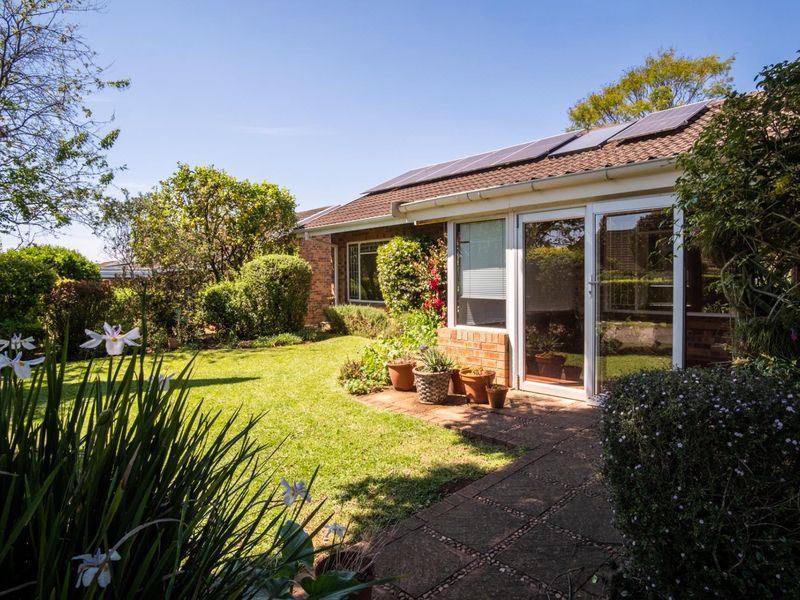 Rear view of the townhouse featuring a well-maintained garden, paved walkway, sliding glass doors, and roof-mounted solar panels.