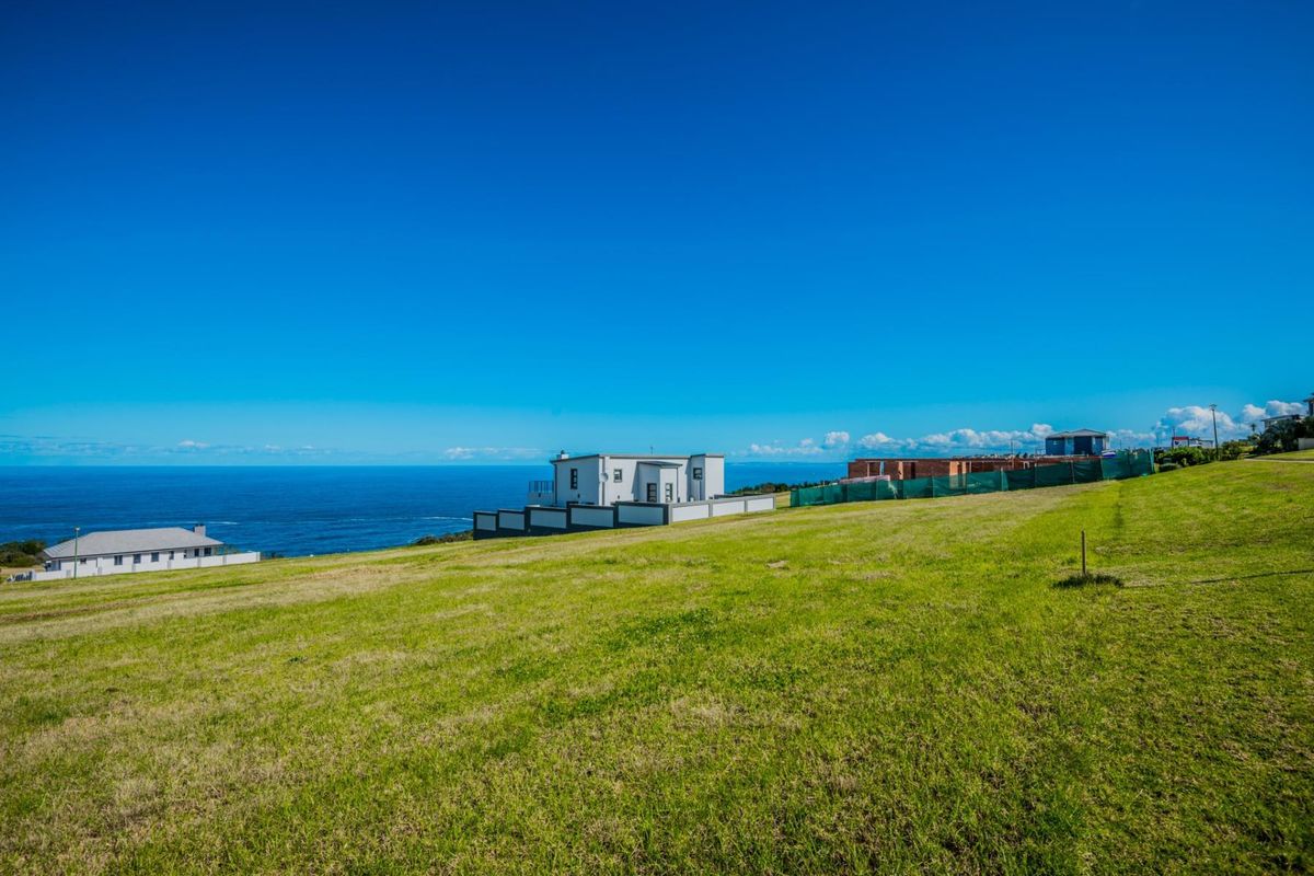 A wide-angle view of a vacant residential plot featuring expansive green lawns and a scenic coastal outlook.
