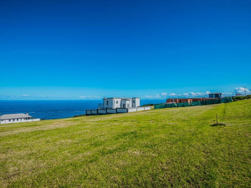 A wide-angle view of a vacant residential plot featuring expansive green lawns and a scenic coastal outlook.