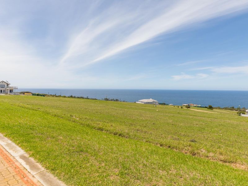A vacant residential plot featuring expansive ocean views, a paved walkway, and established grass, situated in a coastal neighborhood.