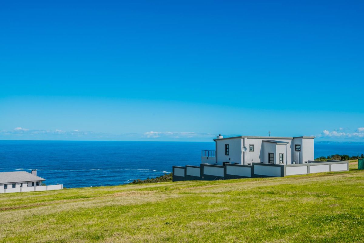 An elevated view of a residential property situated on a grassy plot overlooking the ocean.