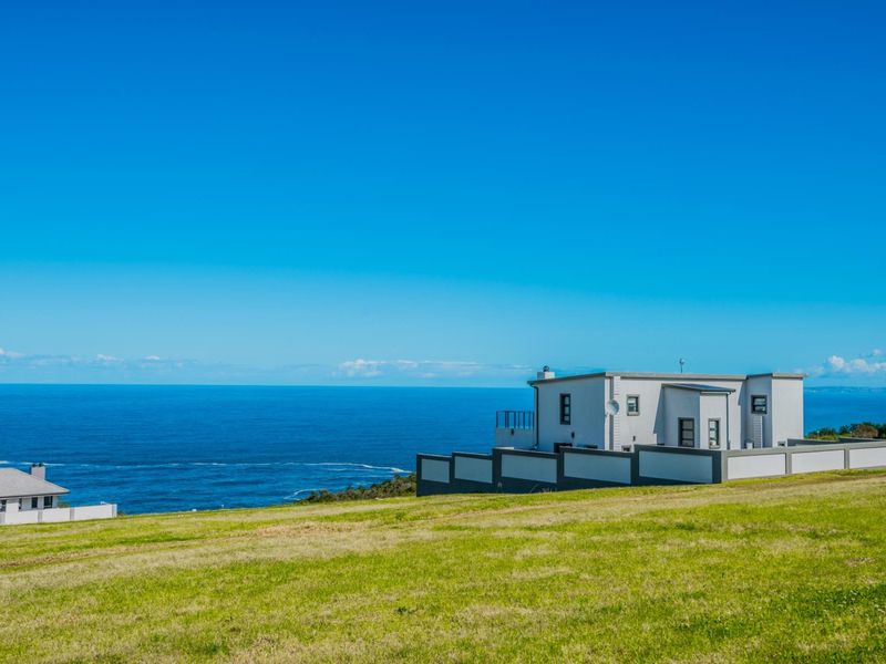 An elevated view of a residential property situated on a grassy plot overlooking the ocean.