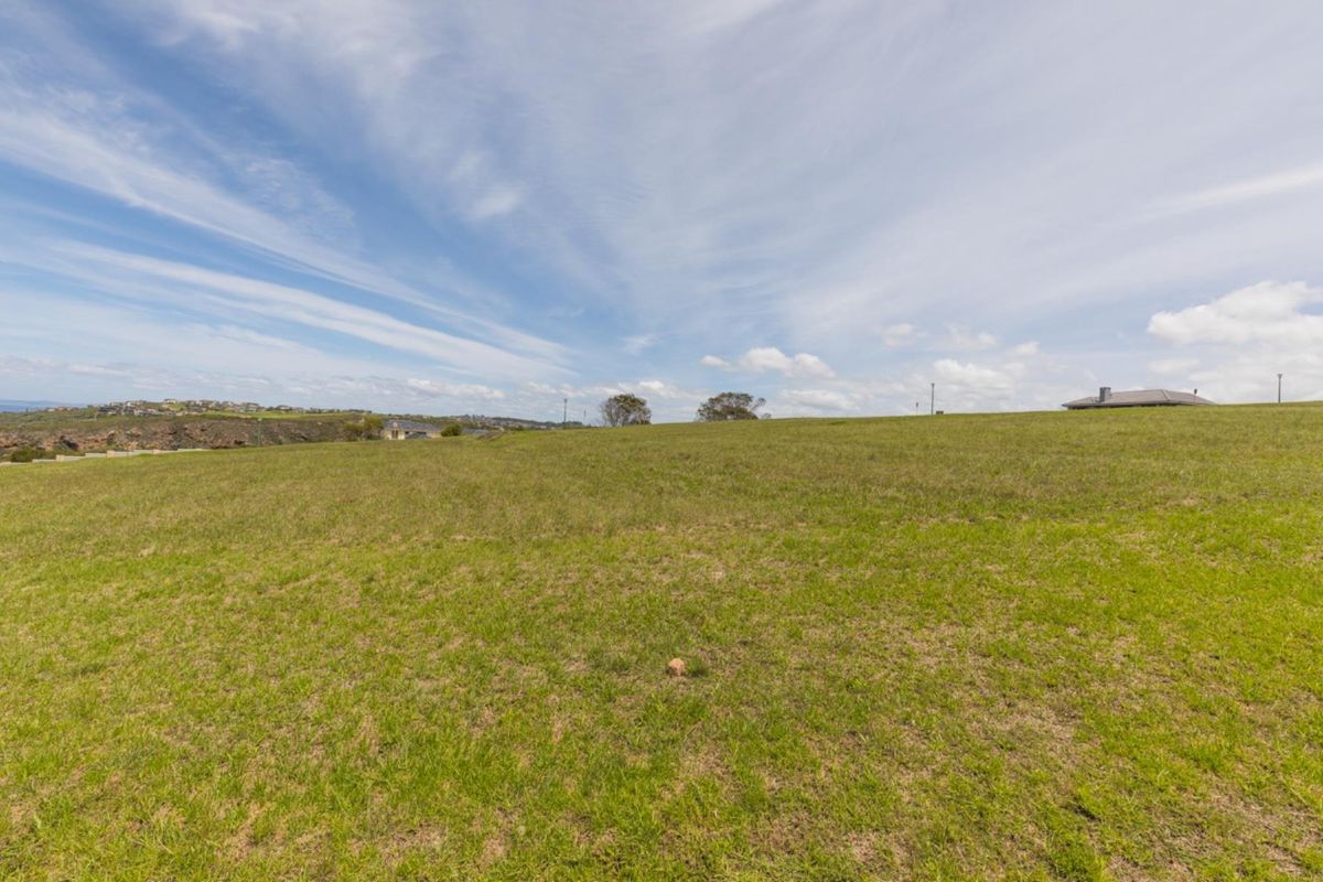 A wide-angle view of a vacant residential plot featuring open grassland and a gentle slope, suitable for future development.