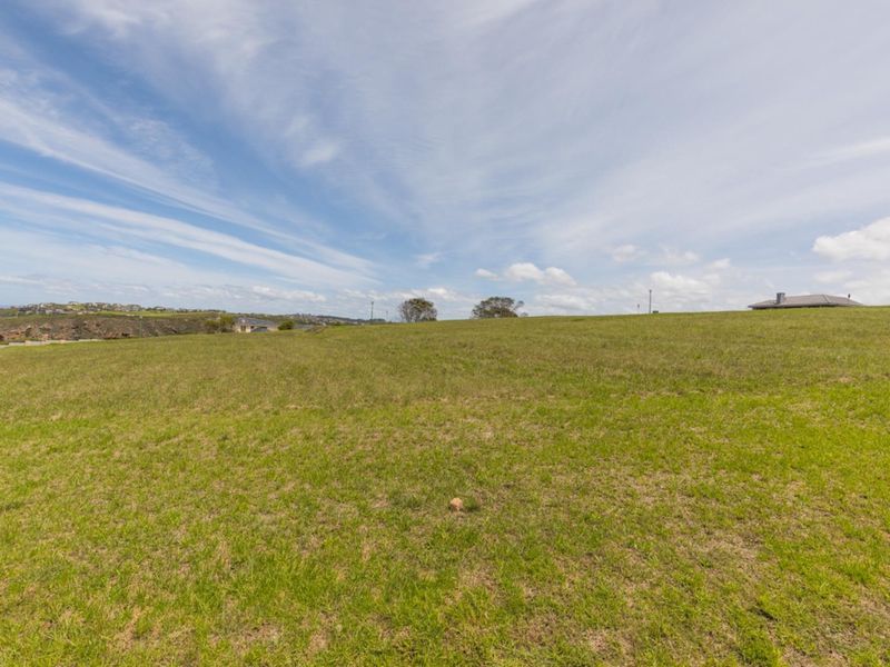 A wide-angle view of a vacant residential plot featuring open grassland and a gentle slope, suitable for future development.