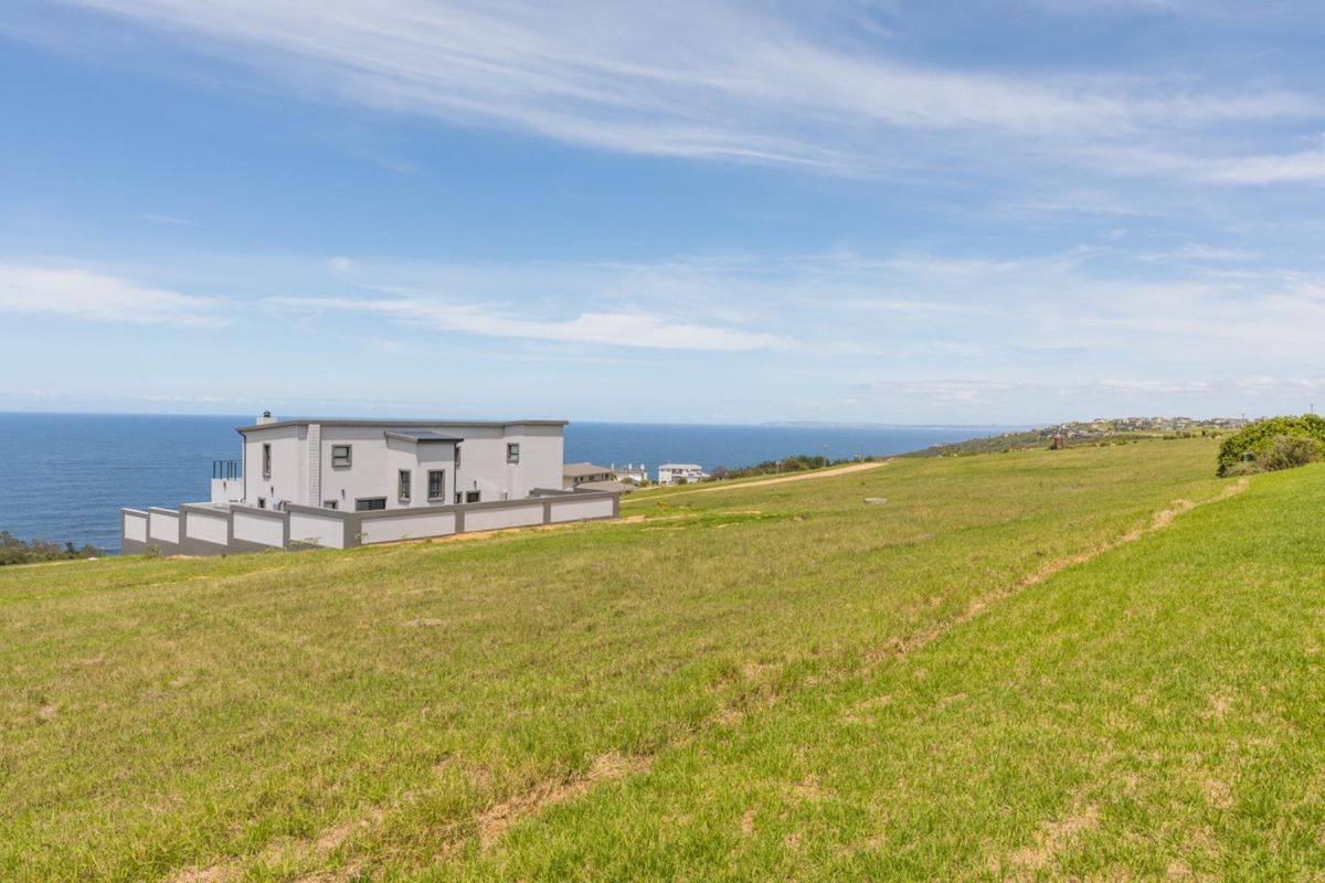 A view of a vacant residential plot featuring expansive grassy terrain and a clear view of the adjacent coastal property and ocean.