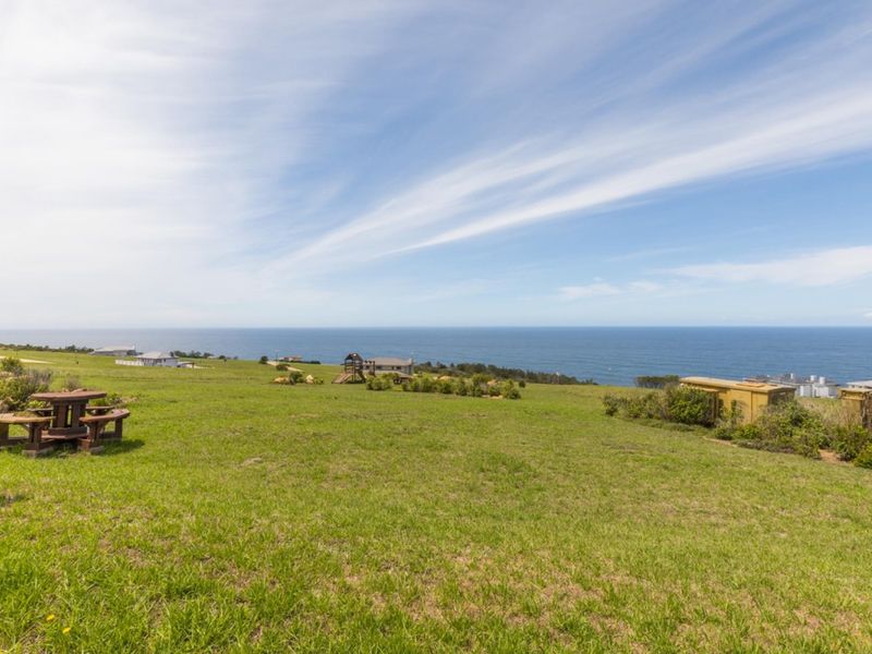 A wide-angle view of a grassy residential plot overlooking the ocean, showcasing the expansive coastal landscape and natural terrain.