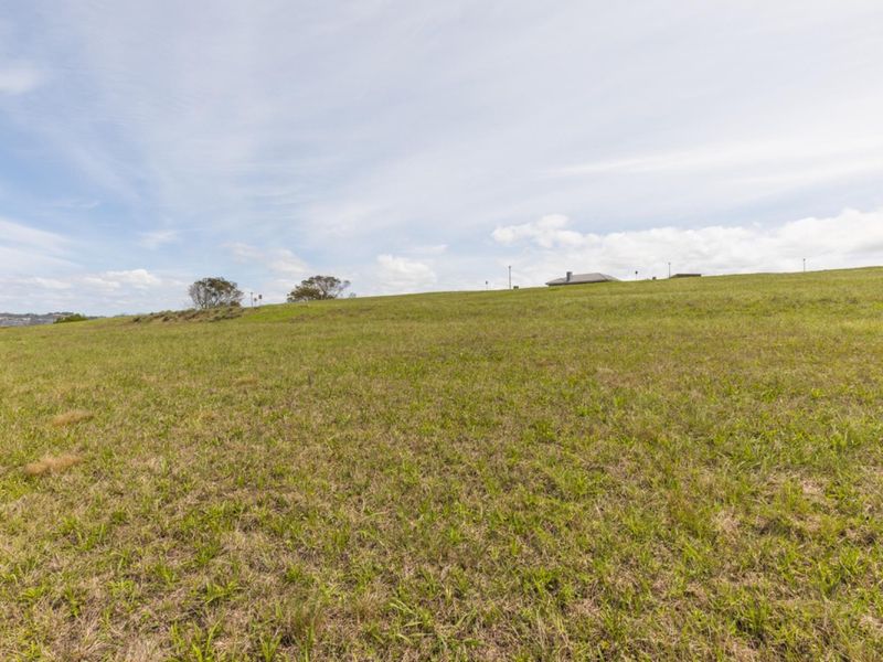 A wide-angle view of a vacant residential plot featuring gently sloping grassland under a clear sky.