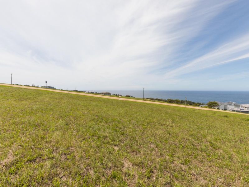 A wide-angle view of a sloping residential vacant land plot overlooking the ocean and coastline.