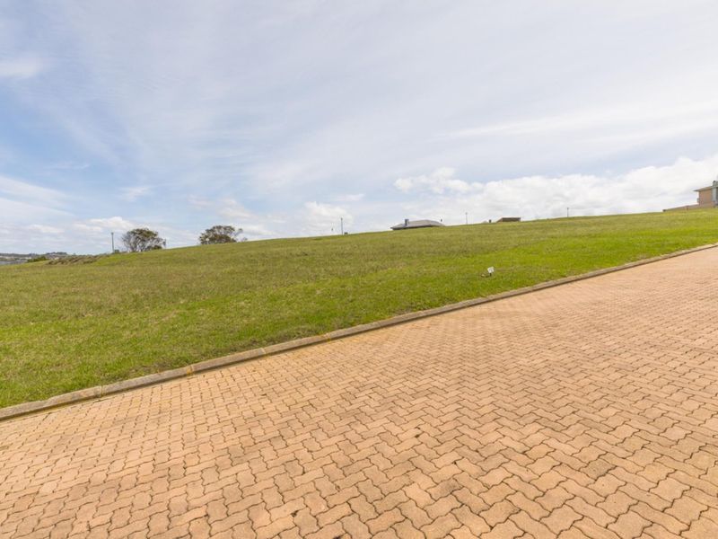 A view of a vacant residential plot featuring a paved driveway and established grass verge.