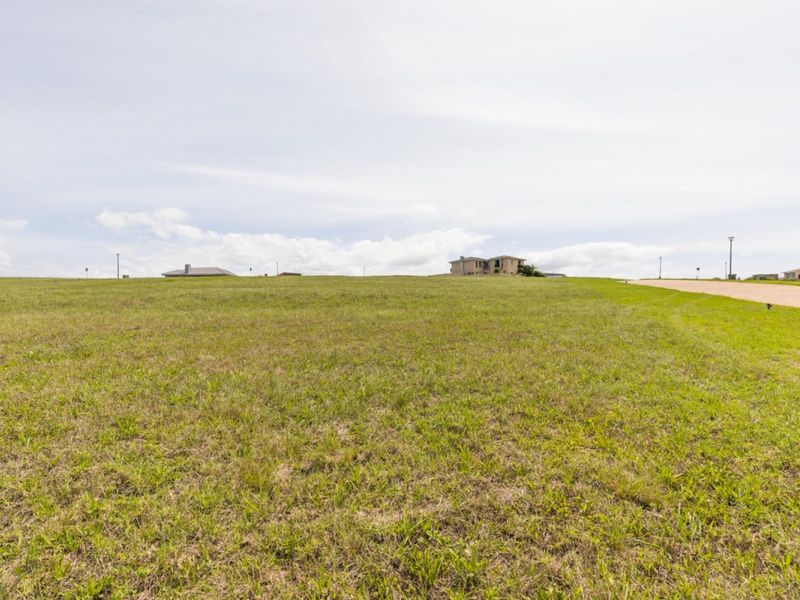 A wide-angle view of a vacant residential plot featuring open grassland with street access, suitable for future development.