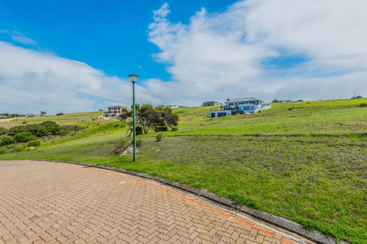 A view of a vacant residential plot from the paved street, featuring established curbing and a street lamp in a coastal neighborhood setting.