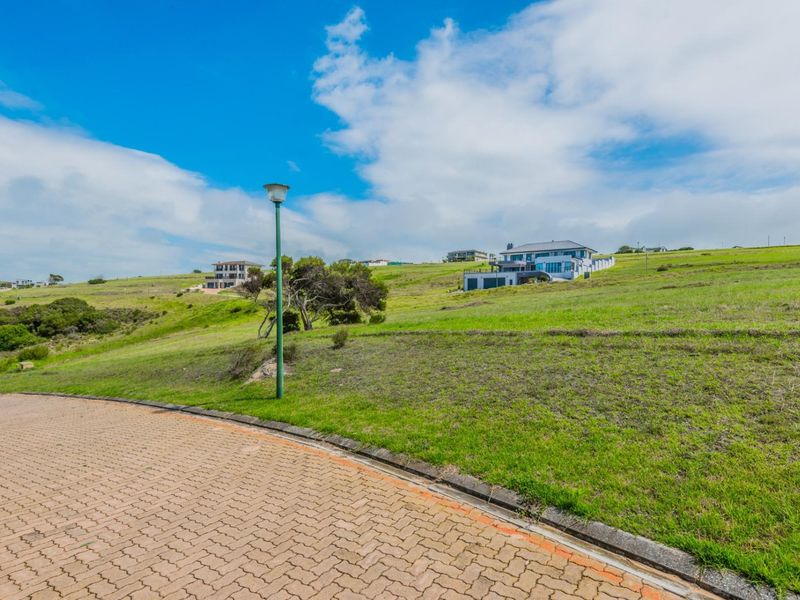 A view of the vacant residential land featuring a paved driveway, street lighting, and surrounding grassy landscape in a coastal estate setting.