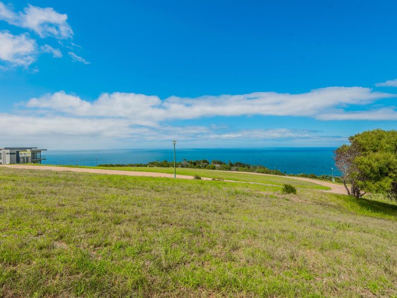 A scenic view of the ocean from a vacant residential plot featuring natural grass and an unpaved access road.