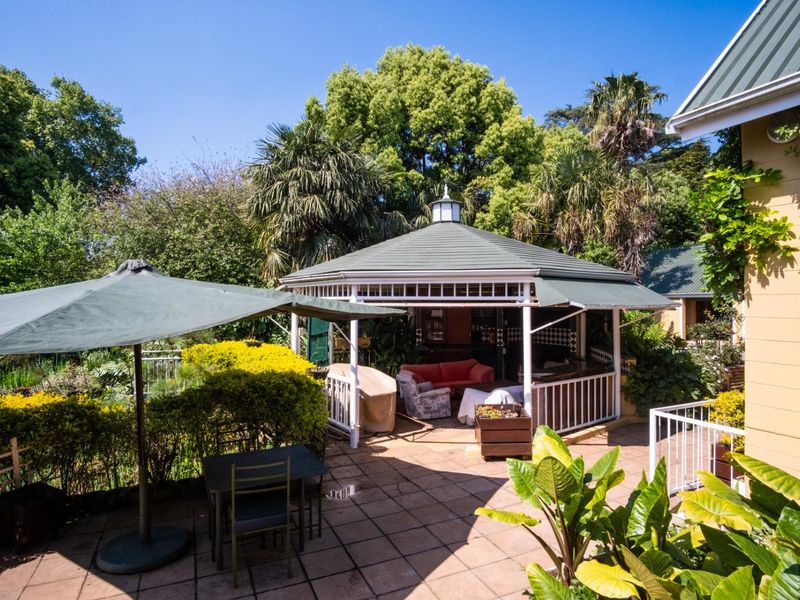 A spacious outdoor patio area featuring a covered gazebo, tiled flooring, and established garden surroundings, ideal for outdoor relaxation and entertainment.