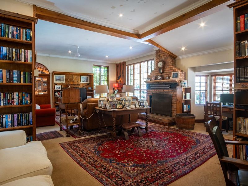 Spacious living room featuring exposed timber ceiling beams, a prominent brick fireplace, and extensive built-in shelving, offering a warm and traditional aesthetic.