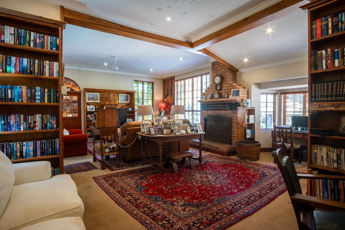 Spacious living room featuring exposed timber ceiling beams, a prominent brick fireplace, and extensive built-in shelving, offering a warm and traditional aesthetic.