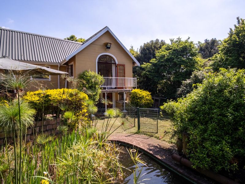 Rear view of the property featuring a landscaped garden with a pond, retaining wall, and an elevated balcony with arched door access.