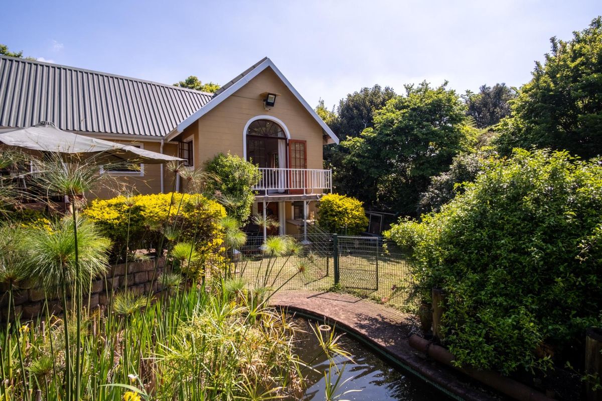 Rear view of the property featuring a landscaped garden with a pond, retaining wall, and an elevated balcony with arched door access.