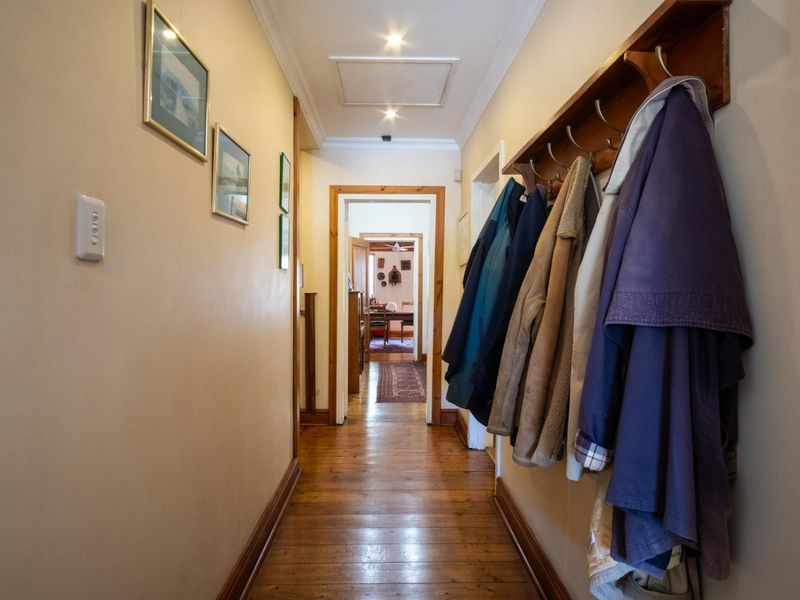 A well-maintained hallway featuring polished timber flooring, recessed ceiling downlights, and classic timber door frames leading to adjacent rooms.