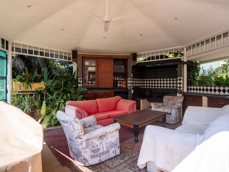 Covered outdoor patio area featuring a built-in braai, tiled splashback, and built-in cabinetry under a vaulted ceiling with a fan.