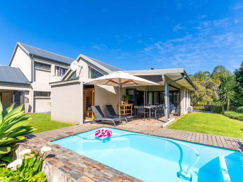 Rear exterior view featuring a swimming pool with stone coping, timber decking, and a covered patio area attached to the main residence.
