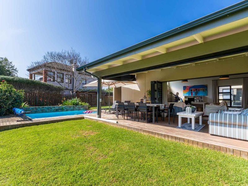 A spacious covered patio featuring timber decking, seamless indoor-outdoor flow through bi-fold doors, and direct access to a private swimming pool and garden.