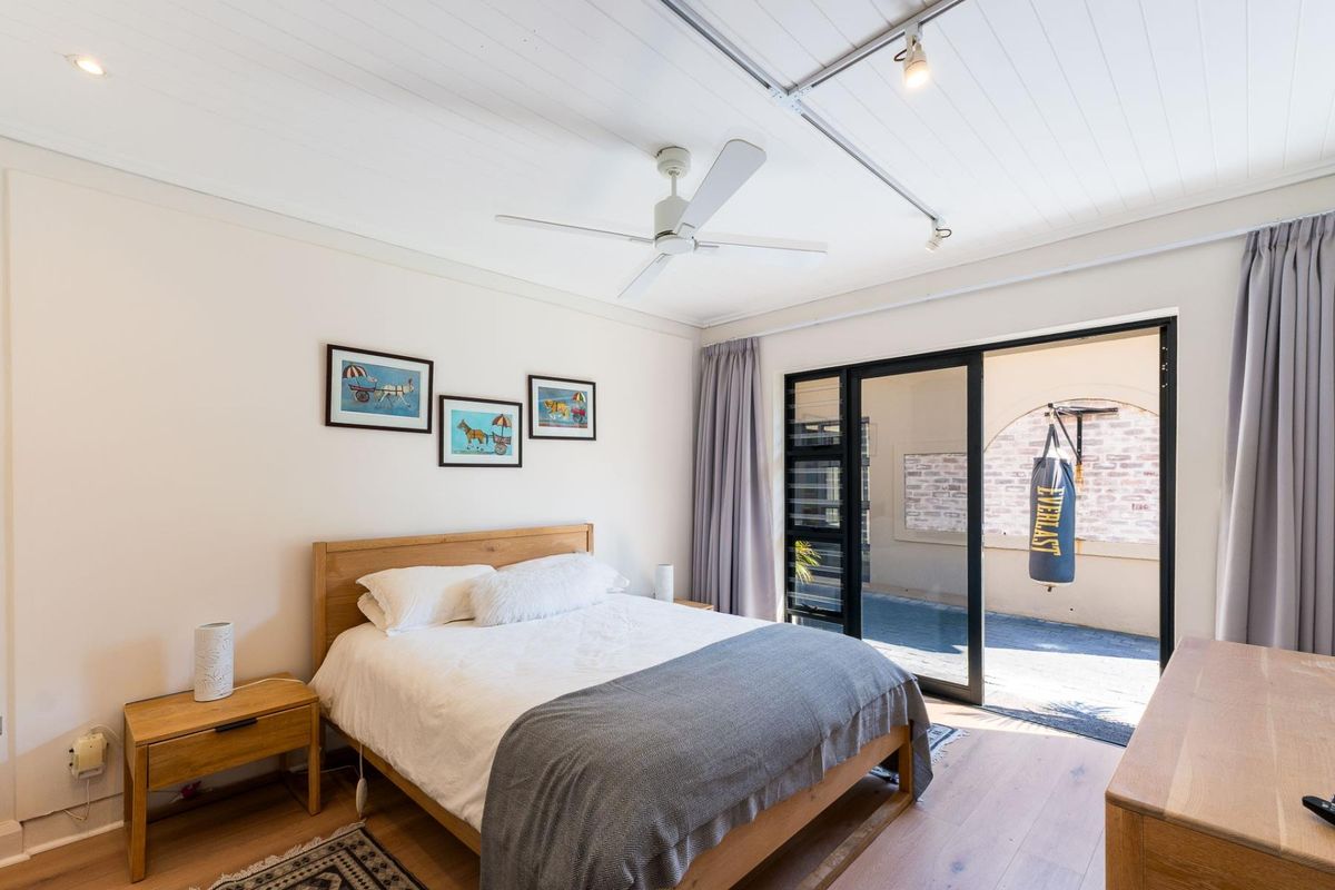 A well-maintained bedroom featuring timber flooring, a tongue and groove ceiling with track lighting, and sliding glass doors opening to an outdoor area.