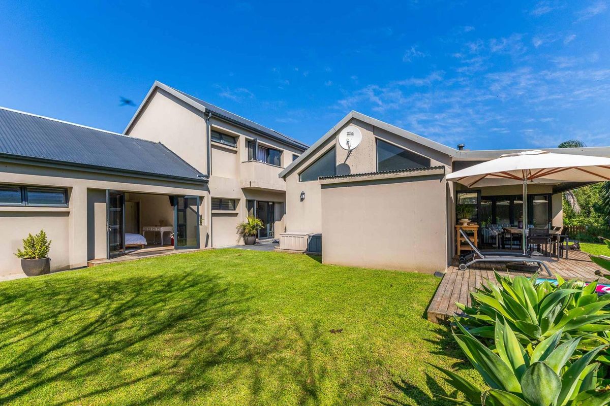 Rear view of the property featuring a well-maintained lawn, timber decking area, and modern architectural design with bi-fold doors.