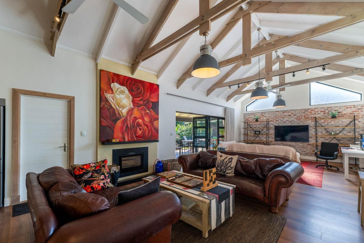 Spacious living room featuring a vaulted ceiling with exposed timber trusses, a built-in fireplace, and an exposed brick wall, opening onto an outdoor patio.