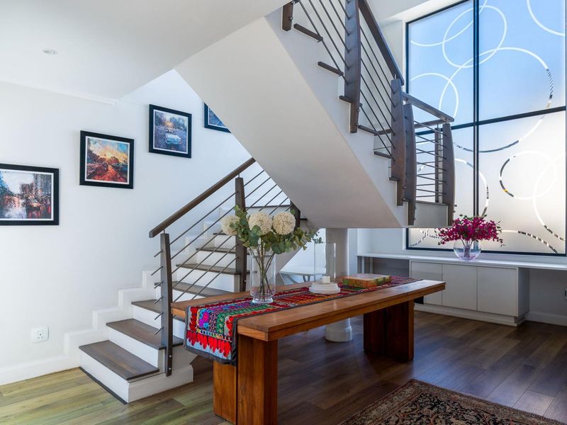 Bright and modern entrance hall featuring a striking staircase with metal balustrades, hardwood flooring, and a large feature window with decorative glass detailing.