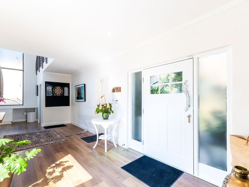 Bright and welcoming entrance hall featuring timber flooring, a classic panelled front door with frosted glass sidelights, and an open staircase.