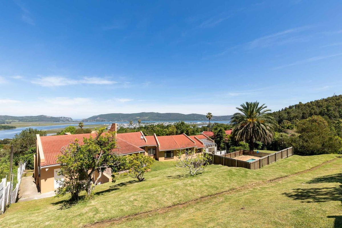 Rear view of the property featuring a terracotta tiled roof, a fenced swimming pool, and expansive lawn with scenic estuary and mountain views.