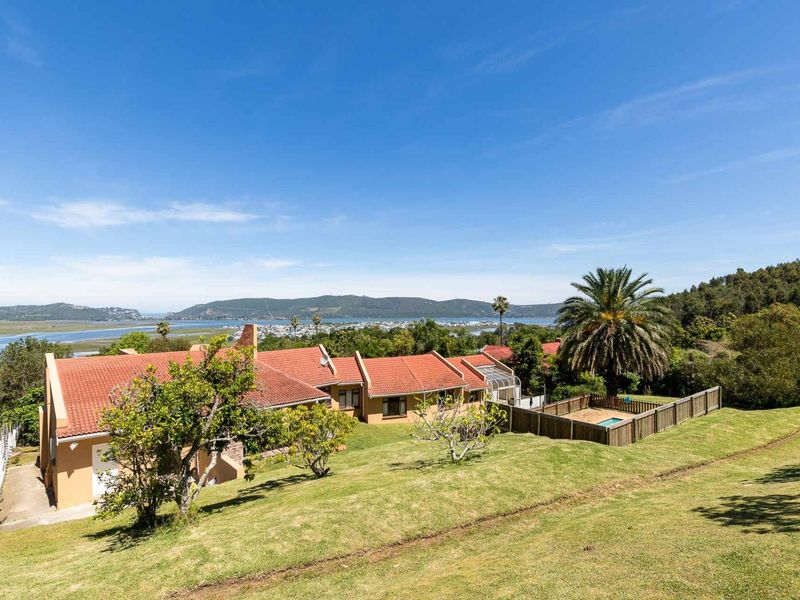 Rear view of the property featuring a terracotta tiled roof, a fenced swimming pool, and expansive lawn with scenic estuary and mountain views.