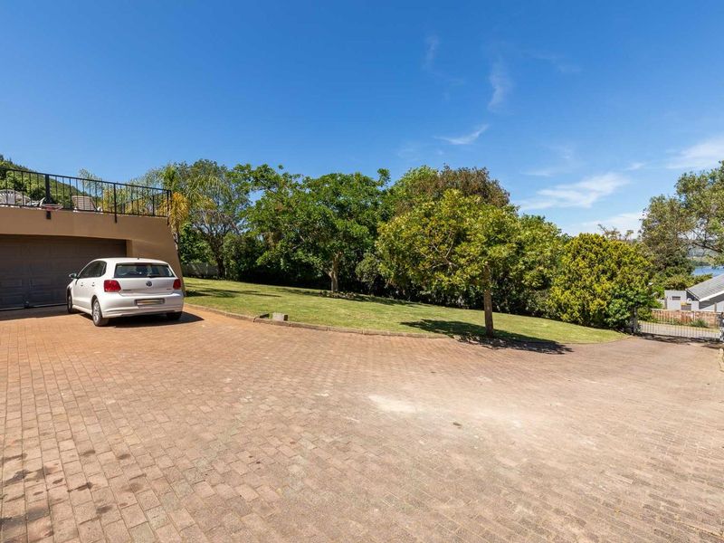Spacious paved driveway leading to a double garage with an elevated balcony area and established garden surroundings.